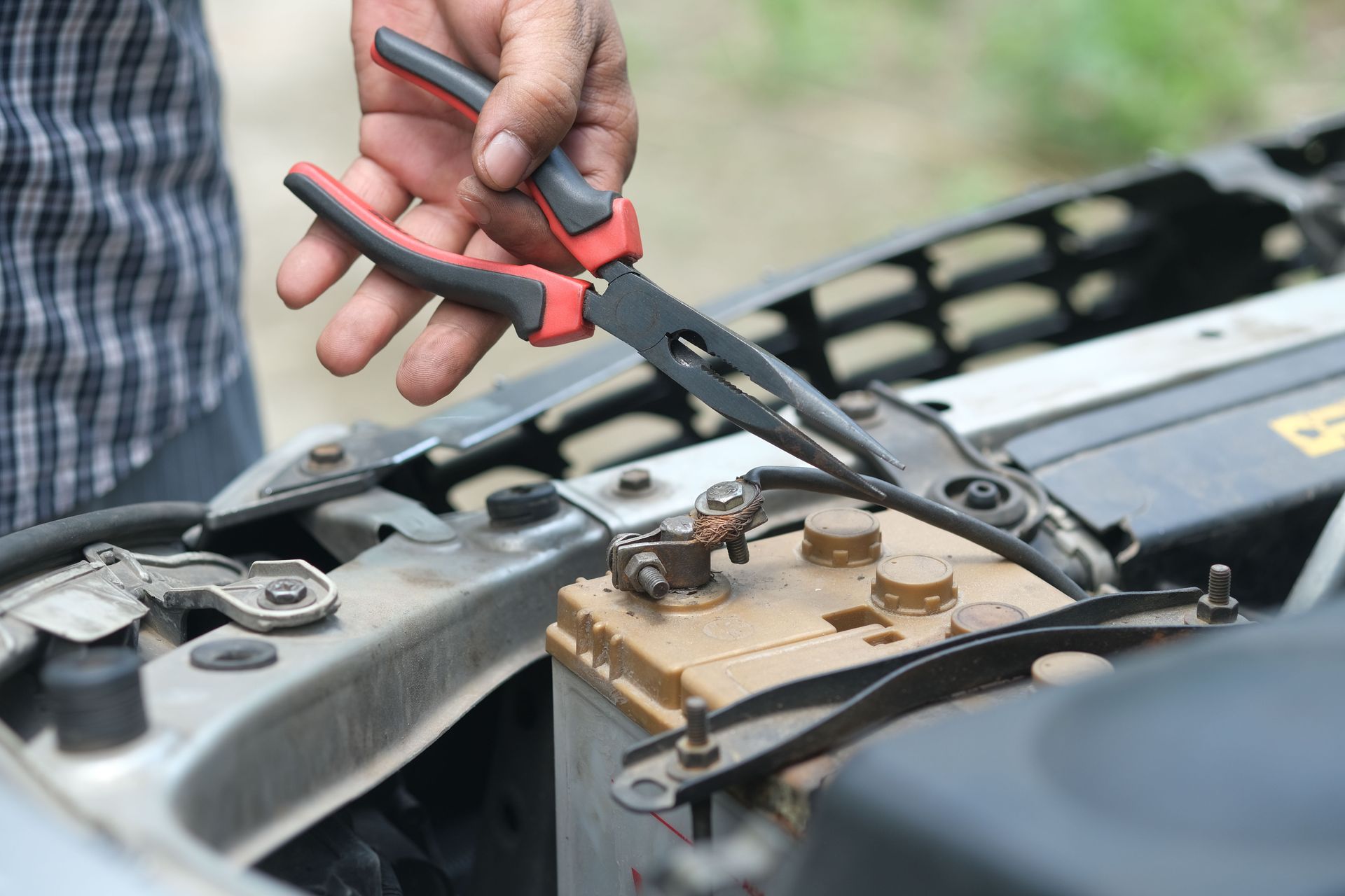 Person using pliers to check a car battery in an outdoor setting.