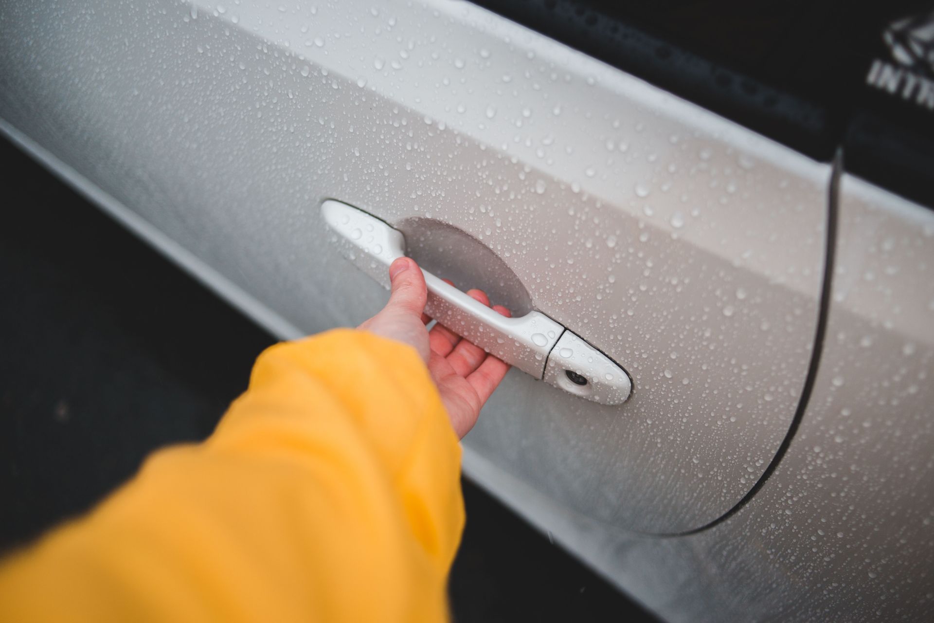 From above of crop unrecognizable person in yellow wear holding handle of modern automobile door with water drips on surface